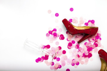 Pink confetti, red women's shoes, and an empty champagne glass on a white background. Concept after party. Morning after the party. Flat lay, top view