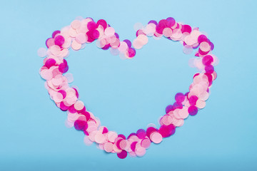 Heart shaped pink confetti on a blue background. Party and holiday concept. Flat lay, top view
