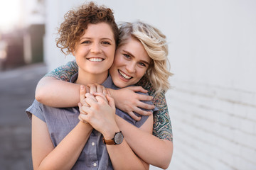 Smiling young lesbian couple standing affectionately together outdoors - Powered by Adobe