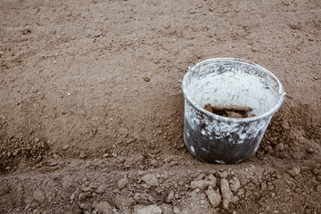 Old bucket covered in paint in the garden between rows with stones and weeds in it after cleaning ground. Work concept, copy space. Film effect.