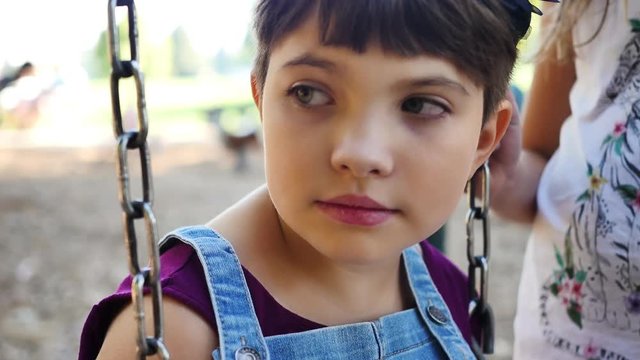 Androgynous girl listens to friend out of frame while sitting on swing