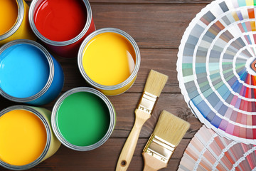 Flat lay composition with paint cans, brushes and color palettes on wooden background