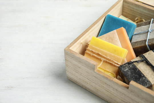 Different handmade soap bars in wooden box on table, closeup. Space for text