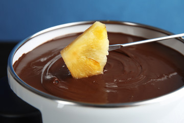 Dipping pineapple into pot with tasty chocolate fondue, closeup