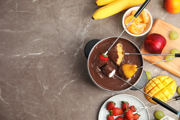 Flat lay composition with chocolate fondue in pot, fruits and space for text on gray background
