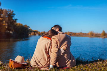 Young couple in love chilling by autumn lake. Happy man and woman enjoying nature and hugging