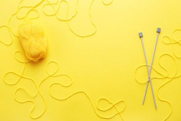 Yellow yarn skein, knitting needles and frame of tangled woolen thread on yellow table. Flat lay,...