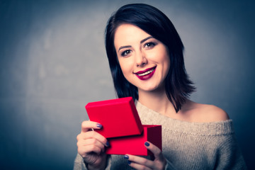 Portrait of a style brunette woman with little red gift box on grey background