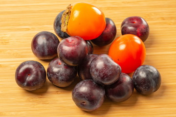 Red plums and orange persimmon fruits close up view isolated on wooden background. Fruits concept. Health concept. Beautiful backgrounds.