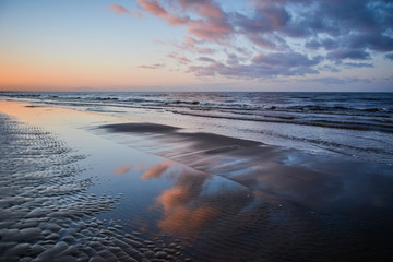 Pink clouds at sunset and reflections in the water at Vakarbulli beach in Latvia.