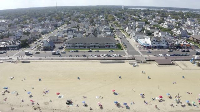 Aerial drone shot over vacationers on the sandy beach with umbrellas and  city buildings in the distance of Belmar, New Jersey.