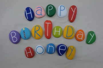 Happy Birthday Honey with colored stones over white sand