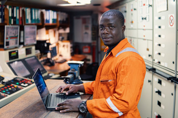 African marine engineer officer in engine control room ECR. Seamen's work. He works at the computer