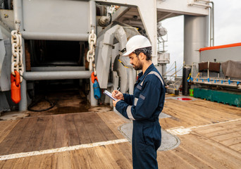 Marine Deck Officer or Chief mate on deck of vessel or ship . He is inspecting and writing...