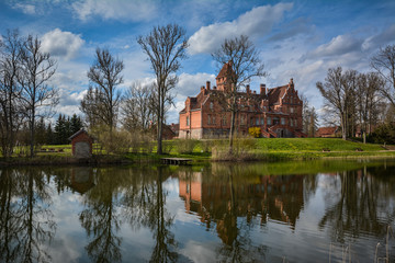 Fototapeta premium Jaunmoku castle near Tukums, Latvia reflecting in the lake. Beautiful blue sky and scenic clouds in the background on a sunny day. Postcard view. Shot in April 2015.
