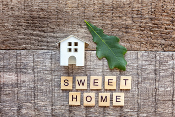 Miniature toy model house with inscription SWEET HOME letters word on wooden backdrop. Eco Village, abstract environmental background. Real estate mortgage property insurance ecology concept