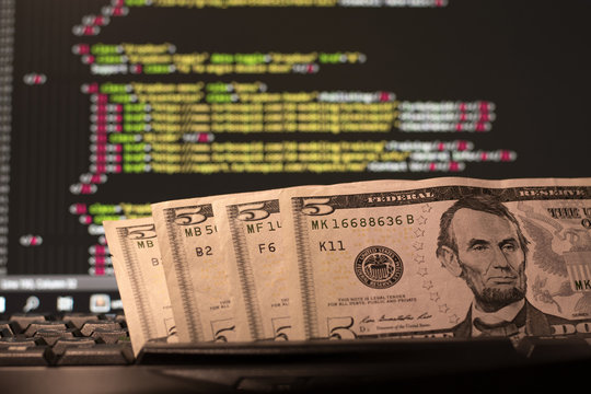 Money on the keyboard and computer display with code on the background