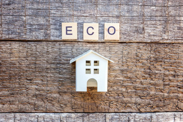 Miniature toy model house with inscription ECO letters word on wooden backdrop. Eco Village, abstract environmental background. Real estate mortgage property insurance sweet home ecology concept