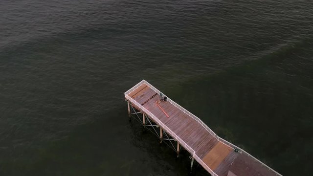 Aerial drone shot over the end of a wooden pier in the green ocean waters off the coast of Belmar, New Jersey.
