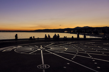Sundial in Nice, France at sunset on Promenade des Anglais with outline of people. A famous place in French Riviera. 