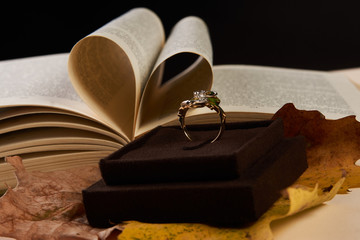 Close-up Jewelry gold diamond ring on autumn foliage and open book pages in heart shape as...