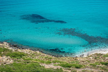 Beautiful turquoise sea and sea shore with few unrecognizable people resting on a sunny summer day. San Giovanni di Sinis, Sinis peninsula, Cabras, Sardinia, Italy.