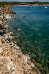 Beautiful turquoise see and cliffs on a sunny clear day with some boats in the background. Captured in Seu Coast, Oristano province, Sardinia, Italy.