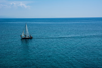 Sailing boat at an open turquoise sea with blue skies on a sunny summer day.