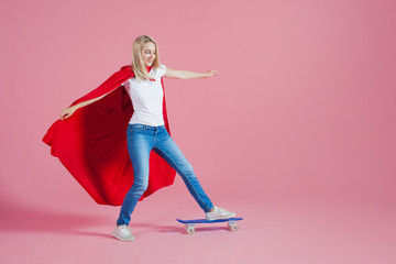 superhero on a skateboard. Funny young woman in the image of a superhero rides a skateboard