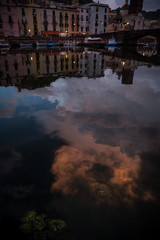 Night city view of Bosa, Sardinia, Italy. Colorful houses and beautiful clouds reflecting in the water after rain at dusk.
