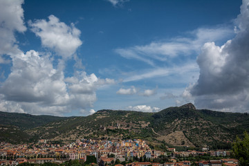 Fototapeta na wymiar City view of Bosa, Sardinia, Italy from above. Colorful houses, mountains and cumulus clouds on a sunny day.