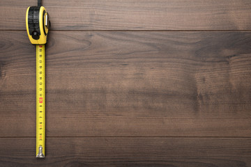tape measure over wooden background with copy space. top view photo of yellow tape mesure on brown...
