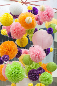Element of decoration made of paper in the interior. Bright decorations of paper colored POM-poms. POM-poms made of paper hanging from the ceiling. Background of colored spots.