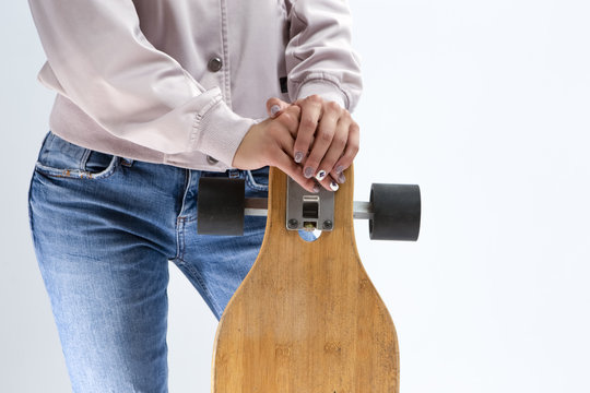 Closeup of hands of Caucasian Girl in Pink Hoodie Holding Longboard In Front. Against White.