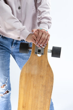 Closeup of hands of Caucasian Girl in Pink Hoodie Holding Longboard In Front. Against White.
