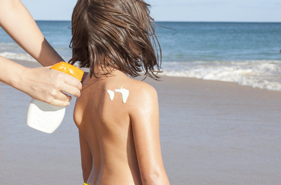Mother applying sunblock cream with spray gun to her daughter on back