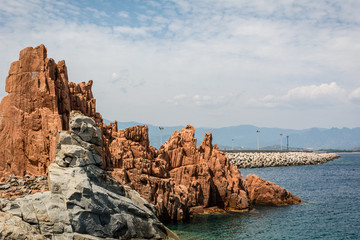 Red rocks of Arbatax city, Sardinia, Italy. Pier, beautiful blue sky with some clouds and sea on a sunny summer day. Nobody in the scene.