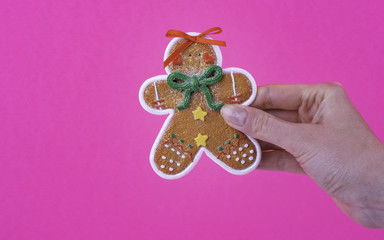 Gingerbread Men Cookie covered colorful ornaments  in woman's hand on pink fuchsia color background. Christmas and New Year celebration concept.
