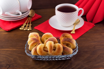 Figured confectionery with fruit filling in a glass plate, tea in a white mug on a red napkin, wooden background.