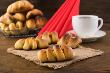 Serving for Breakfast-pastries with fruit filling, tea in a white mug, folded triangle paper napkins, wooden background.