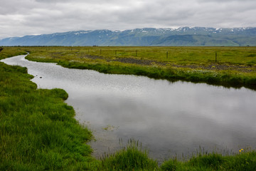Small river with view to mountains on overcast summer day in Iceland.