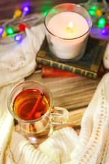 Cozy winter still life: cup of hot tea and books, candle on wooden background and blurred garland lights