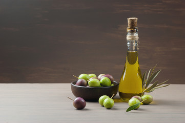 Glass bottle of olive oil and wooden breakfast  bowl with raw  turkish olive seeds and leaves on...