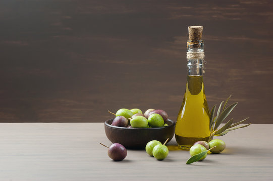 Glass bottle of olive oil and wooden breakfast  bowl with raw  turkish olive seeds and leaves on wooden rustic vintage table. Olives background
