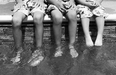 Three boys sitting at the edge of a clear pool with matching bathing suits in black and white