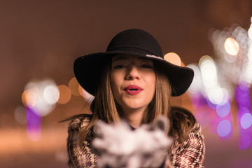 Young girl standing in front on christmas tree lights holding snow in her hands and blowing it. girl on christmass alone in the park