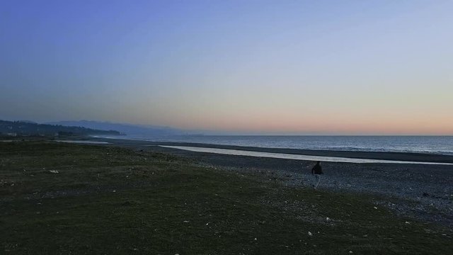 Beach evening view with a man running, sea with chill waves, deep blue sky, Batumi in a distance