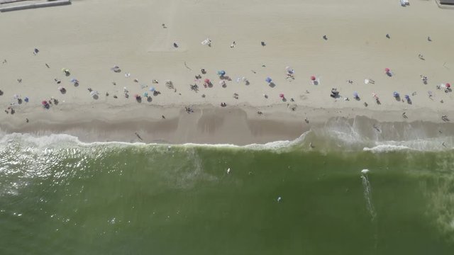 Aerial drone shot over vacationers and beach umbrellas below on the sandy shore of Belmar, New Jersey.