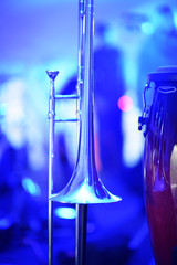 A closeup of a trombone and conga drum under a blue stage light.