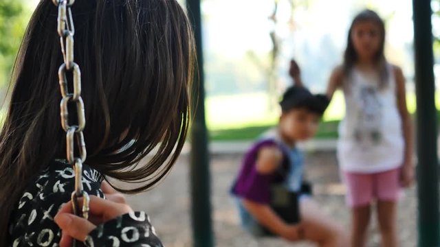 Brunette girl on swing-set has serious conversation with friend on other swing